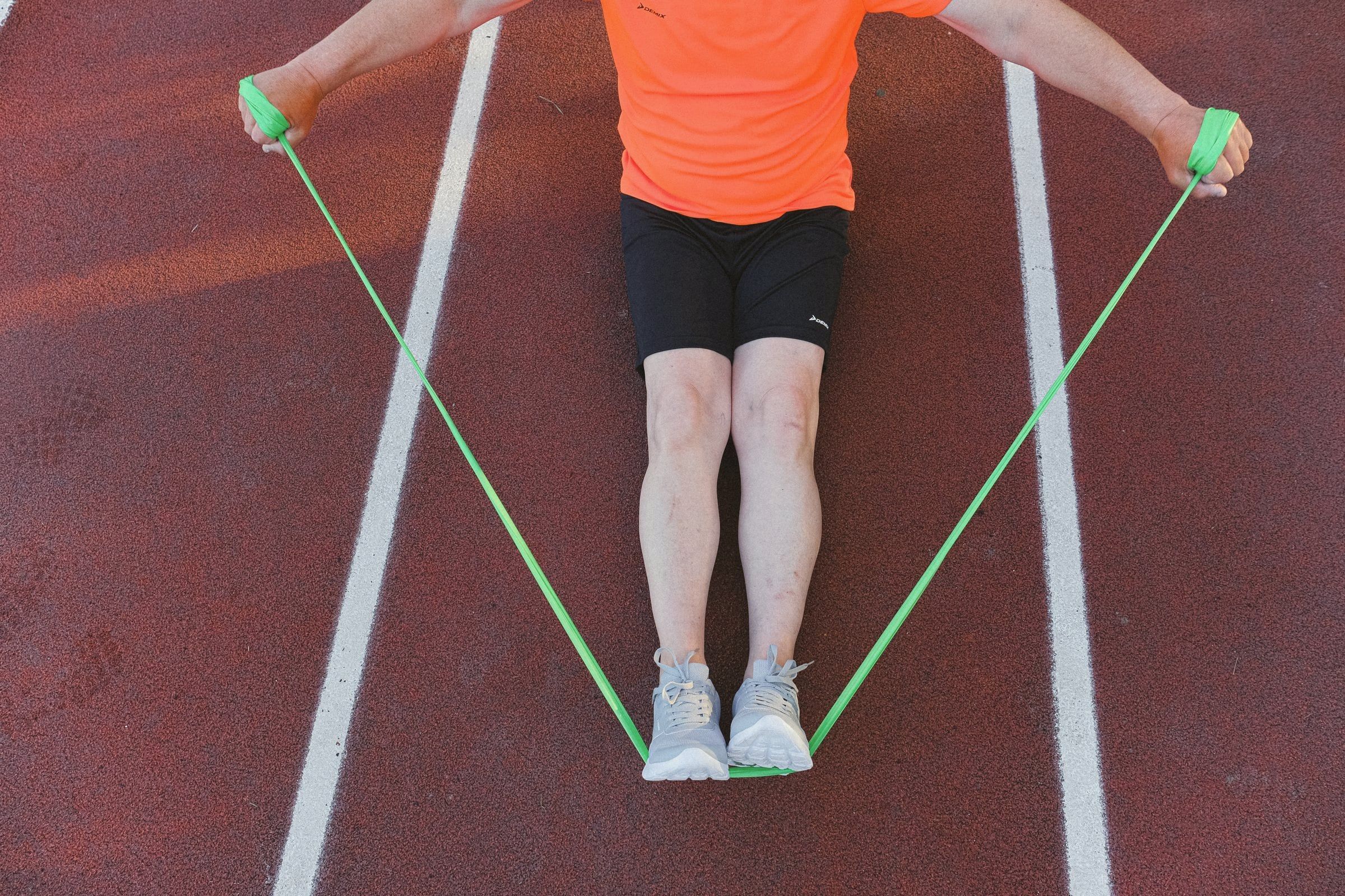 Atleta fazendo exercício de recondicionamento com elástico na pista de atletismo