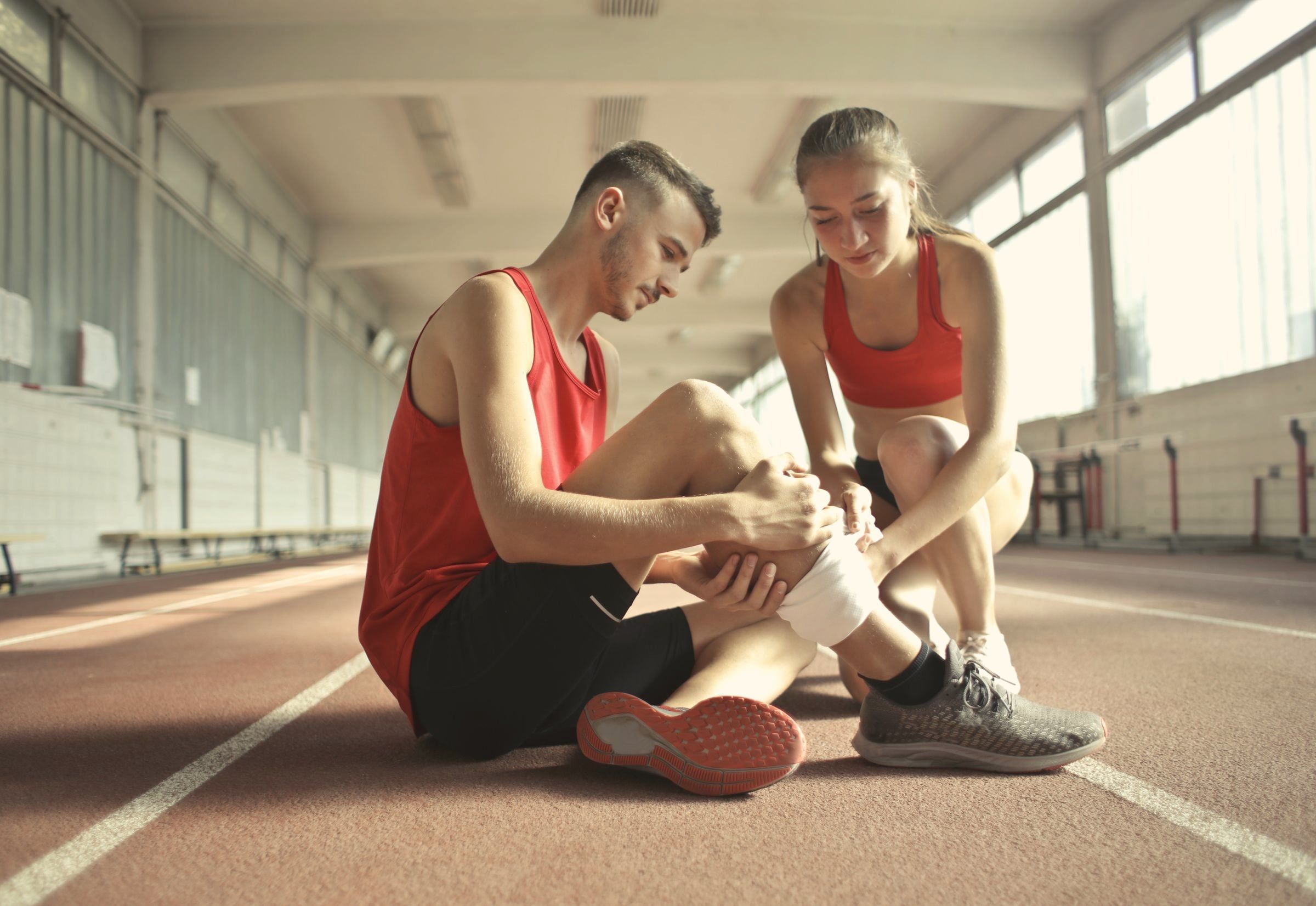 Atleta sentado na pista recebendo bandagem no joelho durante a recuperação de lesão