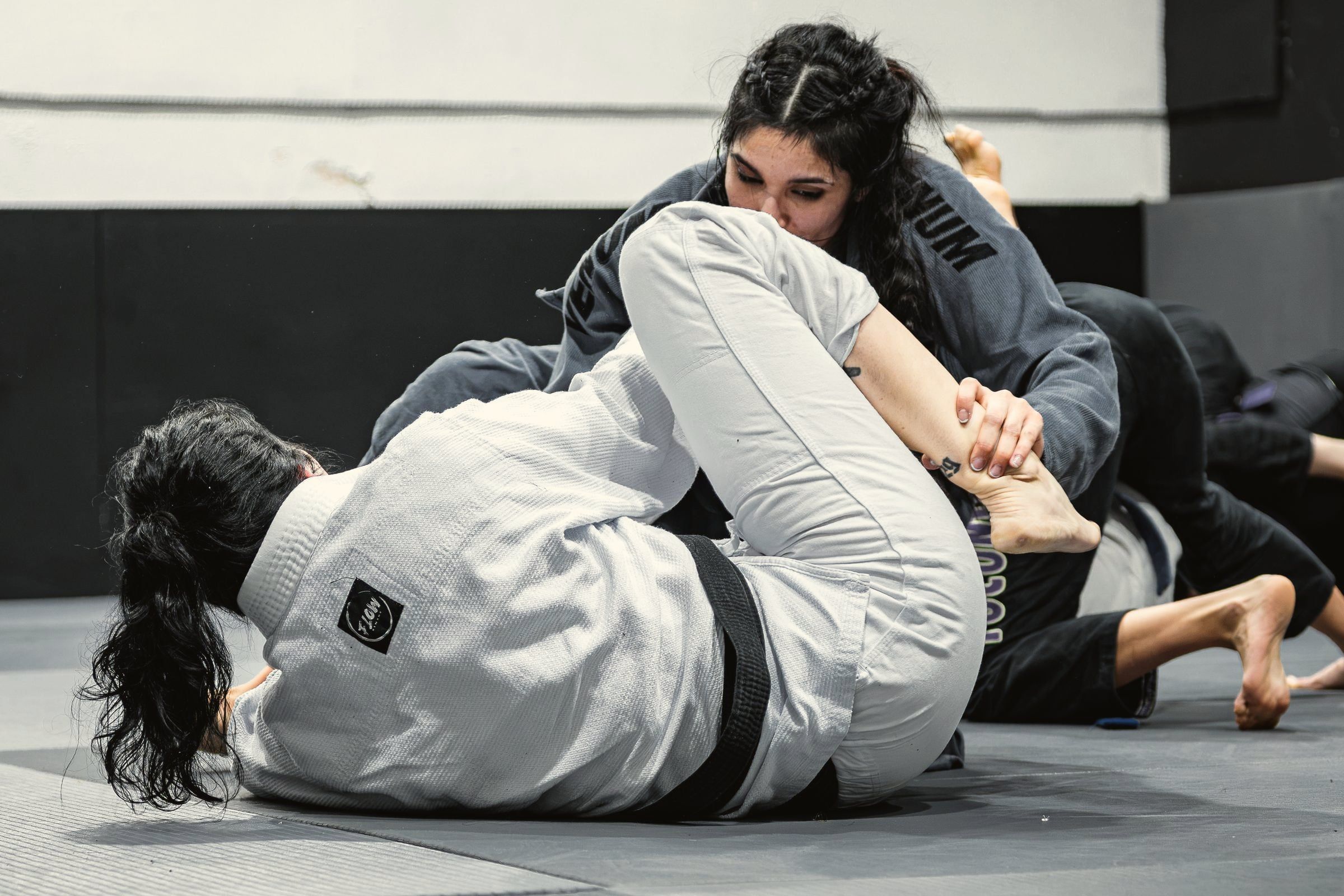 Atletas treinando jiu-jitsu no tatame, uma passando a guarda da outra