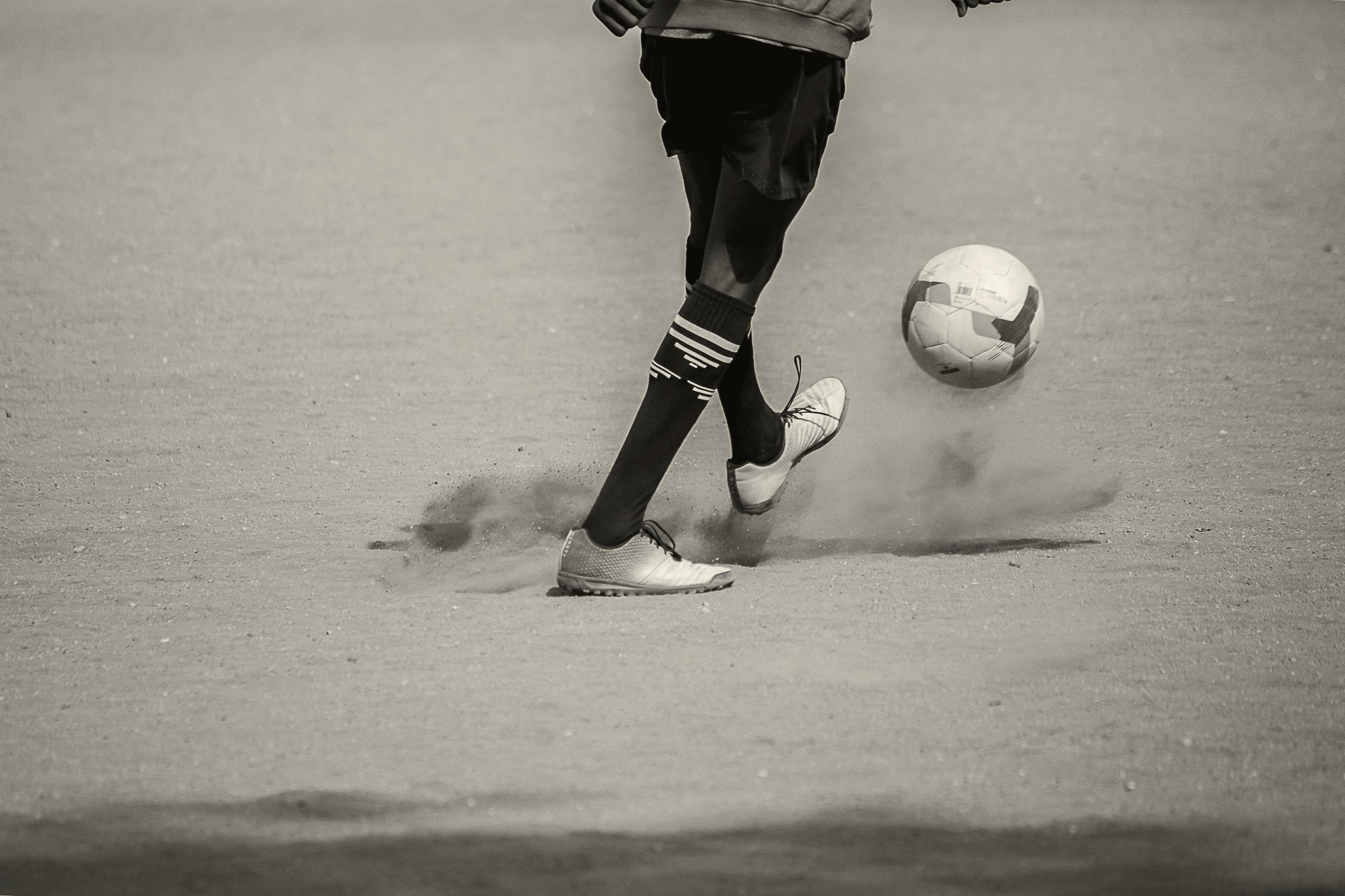 Jogador de futebol chutando a bola, em preto e branco